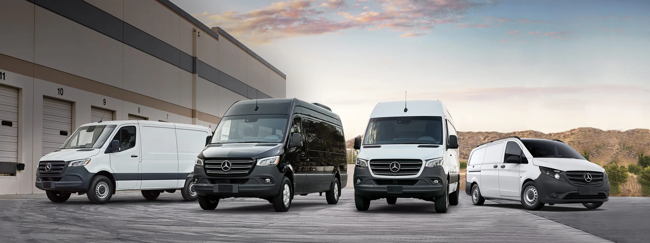 A fleet of Mercedes-Benz Sprinter vans parked outside a service facility at sunset
